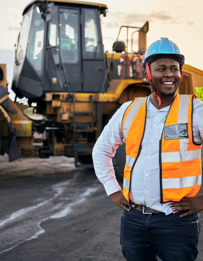 A young Black African coal mine foreman looking off camera laughing wearing reflective bib and hard hat after a long day of work on site at the coal mine